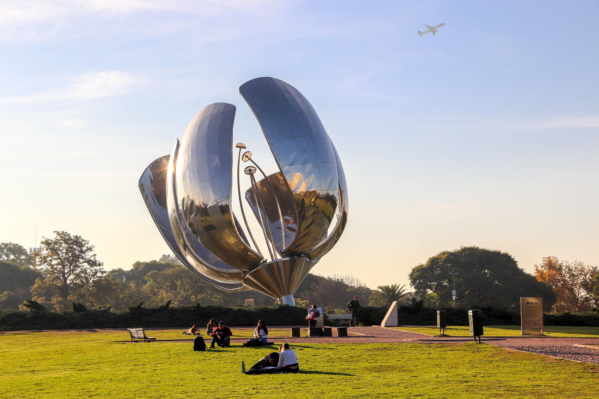Floralis Genérica con la luz del atardecer y un avión en el cielo